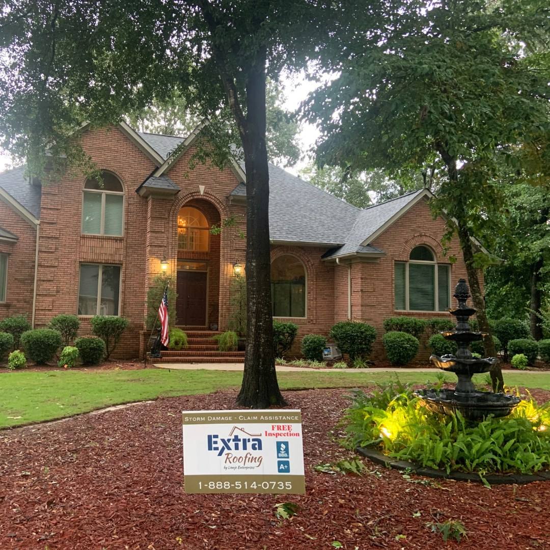 Brick home with a finished roof and an Extra Roofing sign in the yard